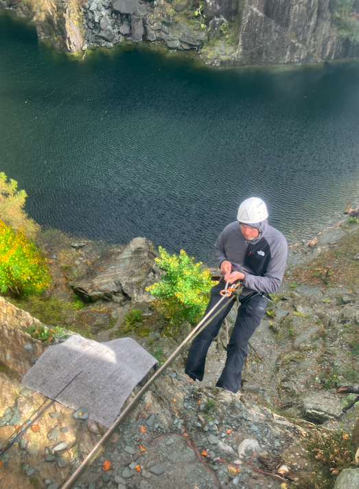 An abseiler descending a rocky face above a Lake District quarry lake