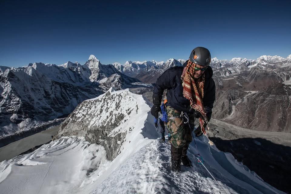 Mountaineer on the summit of Island Peak with the snow ridge and Himalaya behind him