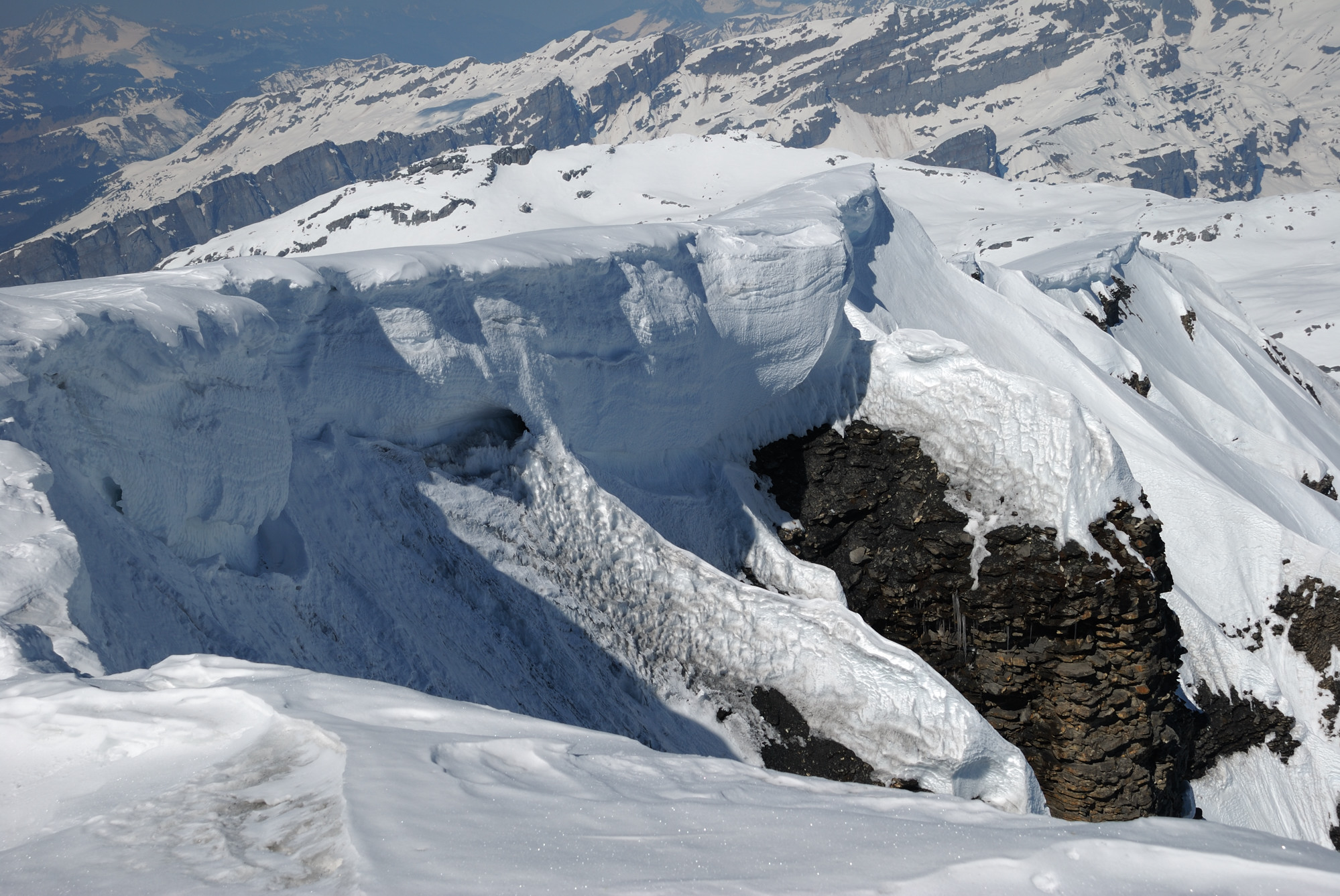 Natural-colour photograph from Mont Buet's snowy summit, showing sculpted snow cornices and the surrounding Alpine mountains