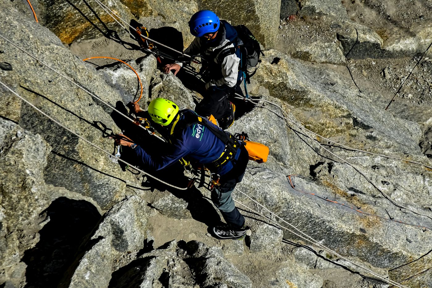Two helmeted climbers working on ropes on a steep rock face