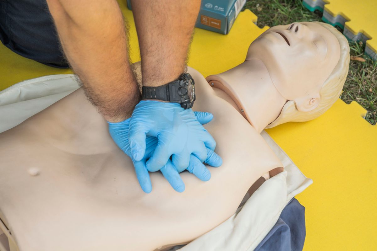 Gloved hands practising chest compressions on a CPR training manikin