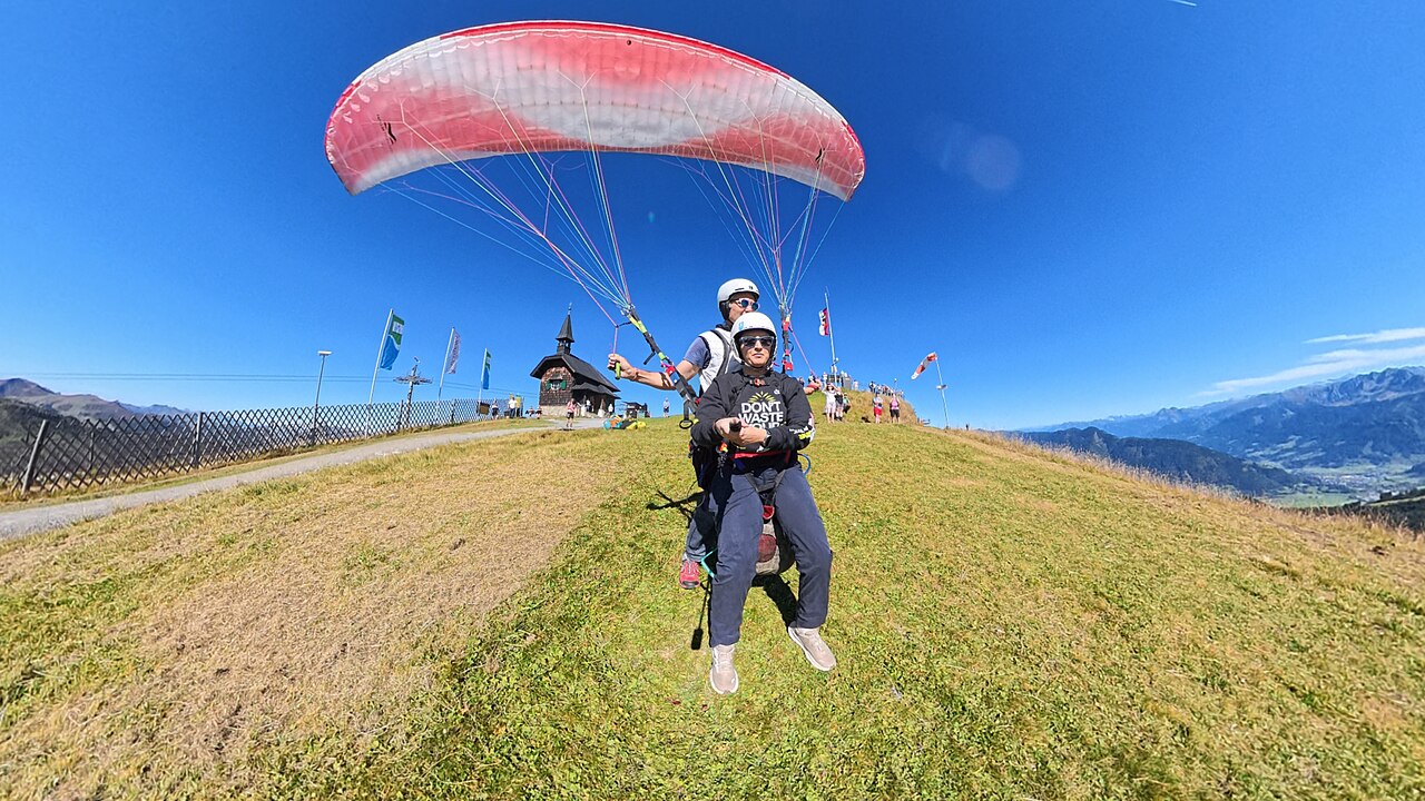 Hajosmit · CC BY-SA 4.0 · https://creativecommons.org/licenses/by-sa/4.0 · https://commons.wikimedia.org/wiki/File:Tandem_paragliding_in_Zell_Am_See.jpg · Displayed cropped to fit Pilot and passenger beneath an inflated tandem paraglider