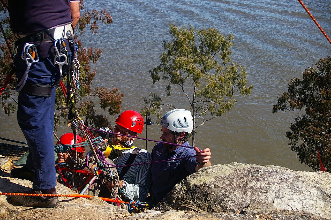 John Robert McPherson · CC BY-SA 4.0 · https://creativecommons.org/licenses/by-sa/4.0 · https://commons.wikimedia.org/wiki/File:NDIS_Promotion_abseiling_Kangaroo_Point_cliffs_River_Tce_Kangaroo_Point_Brisbane_IMGP6094.jpg · Displayed cropped to fit A supported abseil at a cliff edge.