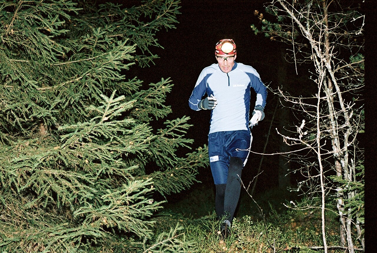 oskar karlin from stockholm, sweden · CC BY-SA 2.0 · https://creativecommons.org/licenses/by-sa/2.0 · https://commons.wikimedia.org/wiki/File:Night-orienteering_by_Oskar_Karlin.jpg · Displayed cropped to fit An orienteer moving through woodland at night with a headtorch