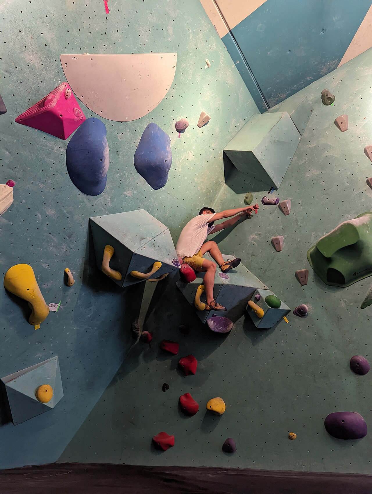 John Kane · CC0 · http://creativecommons.org/publicdomain/zero/1.0/deed.en · https://commons.wikimedia.org/wiki/File:Man_climbing_in_bouldering_gym.jpg · Displayed cropped to fit A climber working on an indoor bouldering problem
