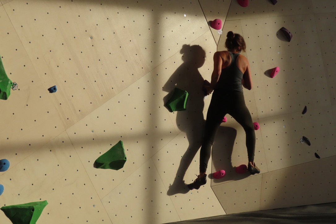 Yvette.Cuthbert · CC BY-SA 4.0 · https://creativecommons.org/licenses/by-sa/4.0 · https://commons.wikimedia.org/wiki/File:Woman_and_her_shadow_climbing_at_the_Winnipeg_Hive_indoor_bouldering_facility.jpg · Displayed cropped to fit Working through a bouldering problem indoors.