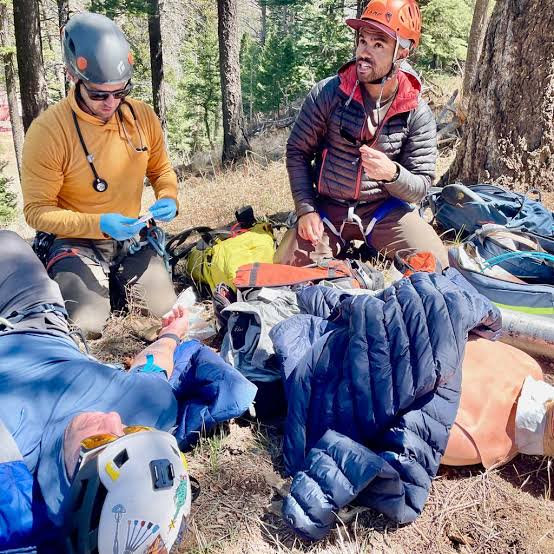 A helmeted outdoor medical team assessing a practice casualty in woodland