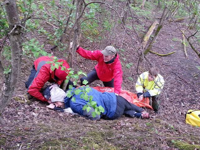 A team practising casualty care on uneven woodland ground